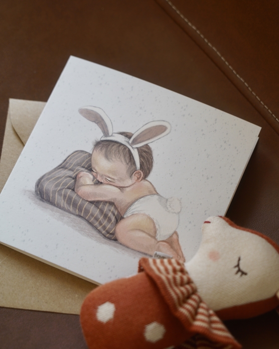 Kartka na narodziny Hi Little, Born to be loved z kopertą. Obok leży grzechotka - jelonek duńskiej marki Maileg.